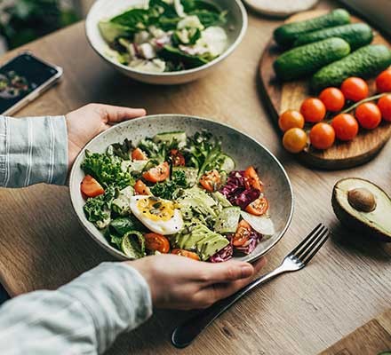A person about to eat a large salad bowl surrounded by fresh produce
