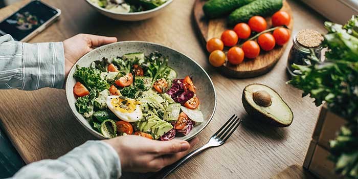 A bowl of salad next to some salad ingredients on a table