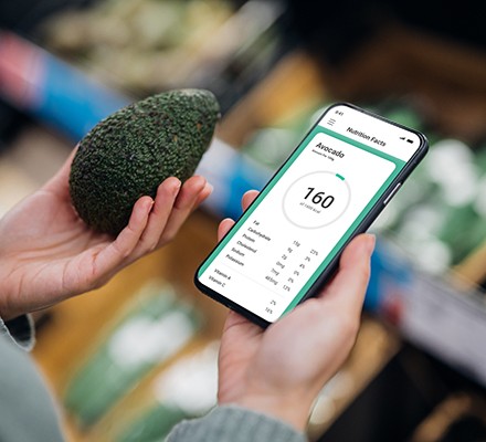What is a calorie deficit? Female hands holding an avocado and a phone with a calorie and nutrition app