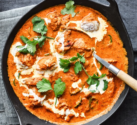 Butter chicken served in a cast iron pan topped with cream and coriander