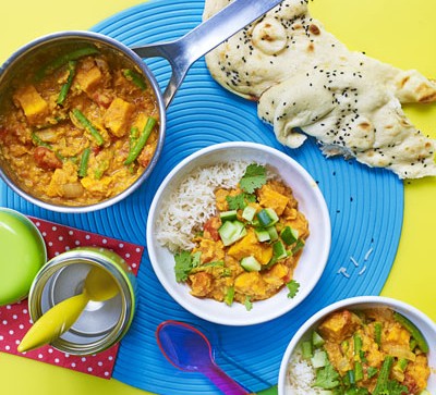 Two bowls and a pot of chunky vegetable curry, with naan bread