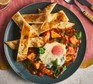 Baked eggs with spinach sit on a plate with cut up slices of naan