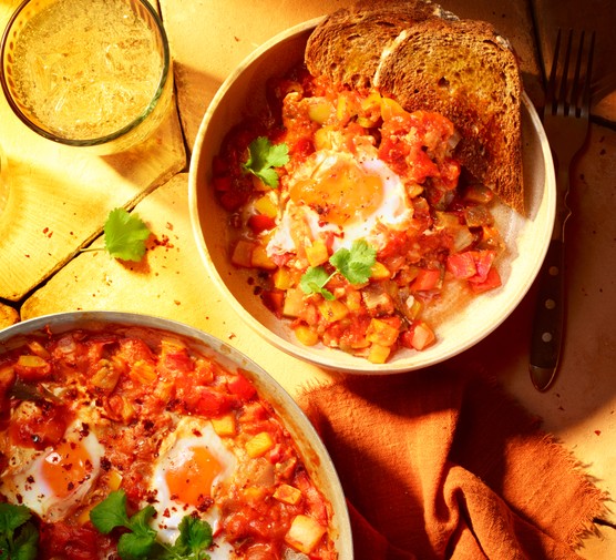 A bowl of shakshuka made from tomato, eggs and vegetables sit in a bowl