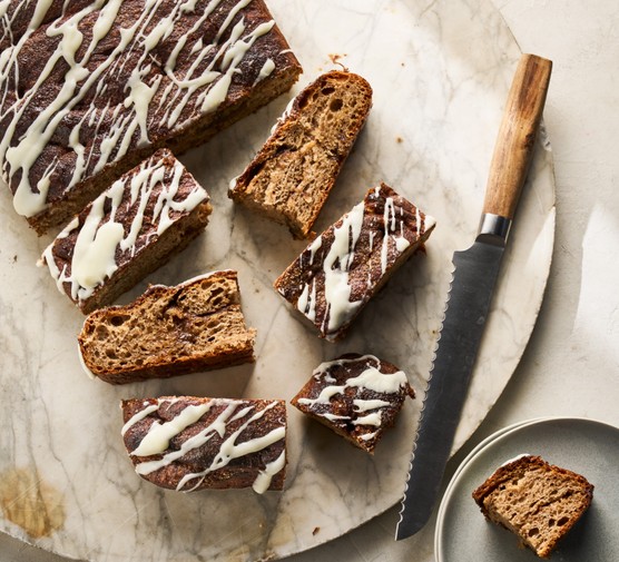 A loaf of cinnamon flavoured bread sits on a board with icing