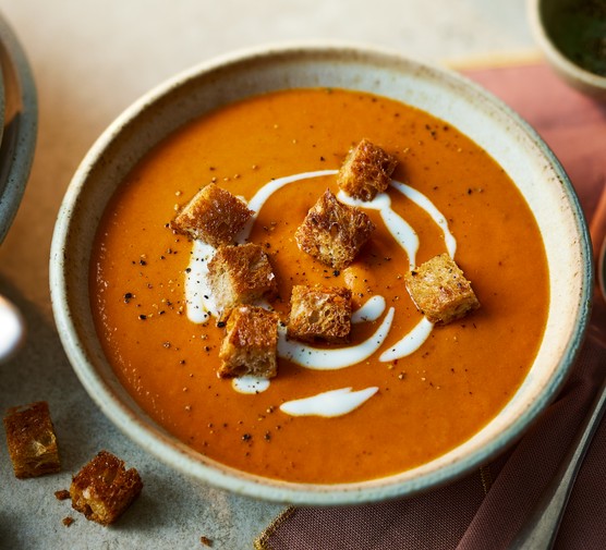 Bowl of red pepper soup topped with yogurt and croutons