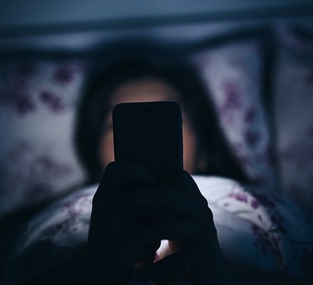 Woman texting and reading on smartphone in bed