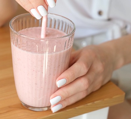 Pink milkshake in a glass being held in female hands