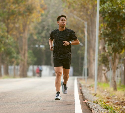 A man in a black T-shirt and shorts running outdoors