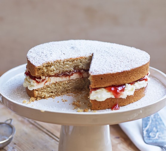 Vegan Victoria sponge cake with slice taken out, on a cake stand