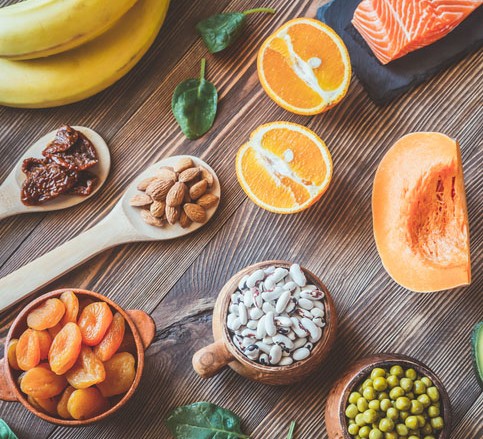 A flatlay of foods that are high in potassium: bananas, nuts, oranges, dried apricots, salmon and melon
