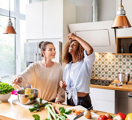 Businesswoman with colleague tasting spaghetti in office kitchen